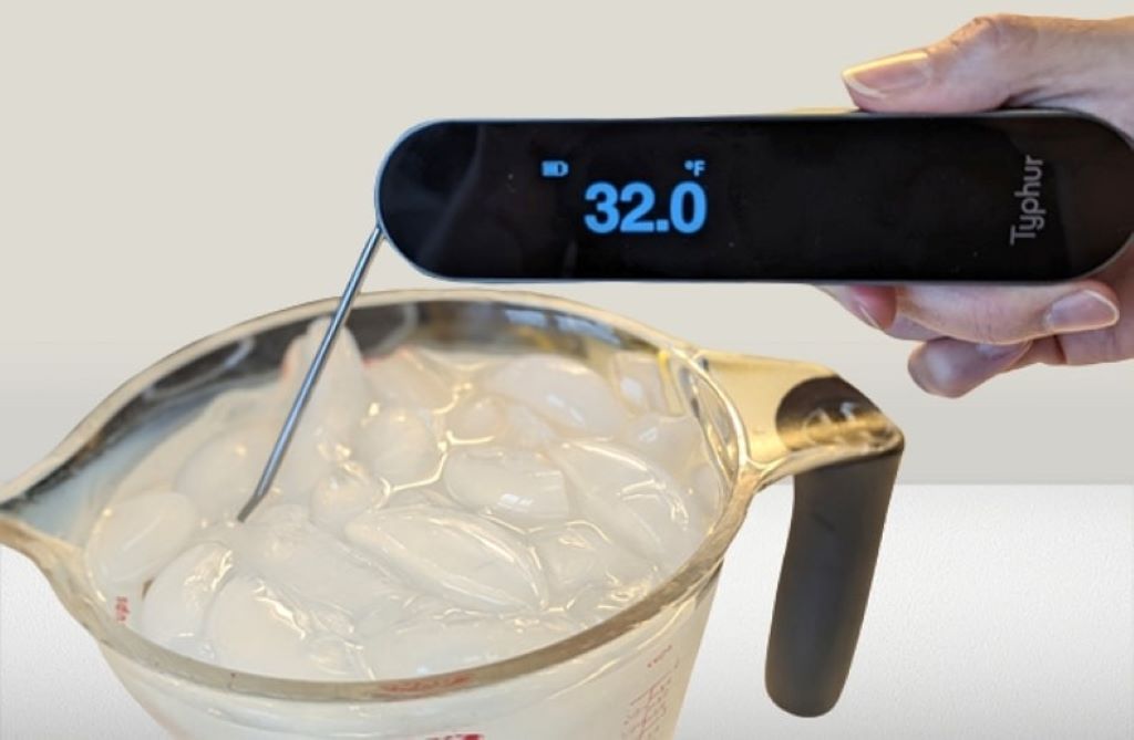 A digital reef tank thermometer probe being placed into an ice bath slurry for calibration