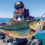 Angler holding smallmouth bass caught using spybait technique in clear river water