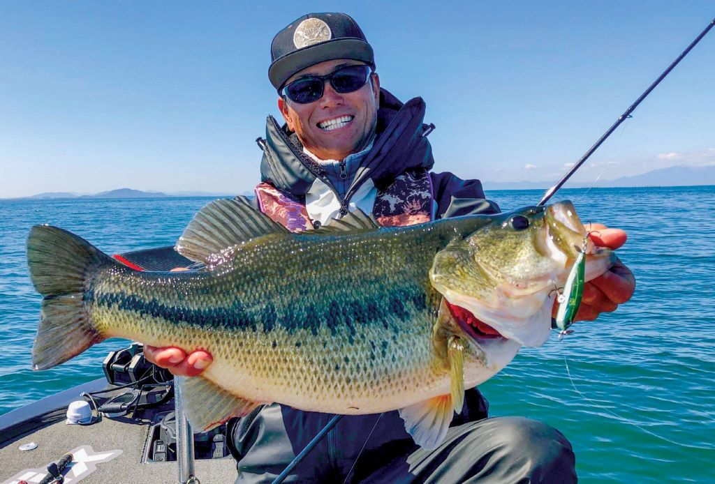 Angler holding smallmouth bass caught using spybait technique in clear river water