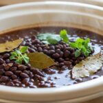 Slow cooker filled with tender cooked black beans in savory broth with bay leaves and herbs