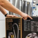 Person comparing vacuum cleaner specifications on product boxes in appliance store showroom