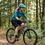A beginner rider on an entry-level hardtail mountain bike on a dirt trail surrounded by trees