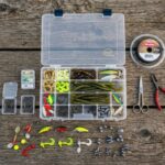 An open plastic budget fishing tackle box sitting on a wooden dock.