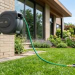 Person installing a heavy-duty retractable garden hose reel on an exterior brick wall.
